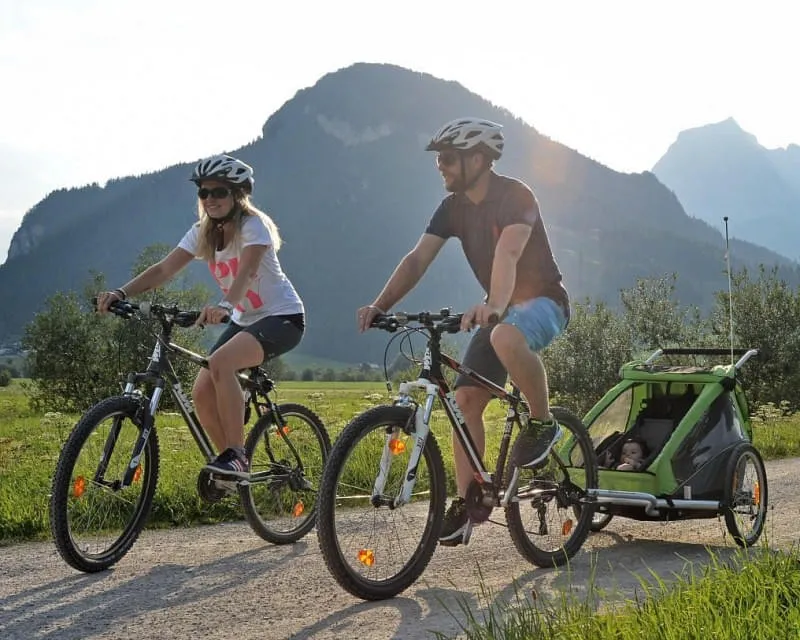 Familie beim Radfahren mit Kinderanhänger und Baby im Tal der Kitzbüheler